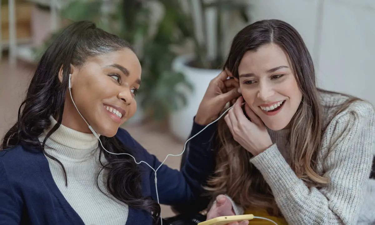 Two ladies enjoy listening to phone tunes on earphones