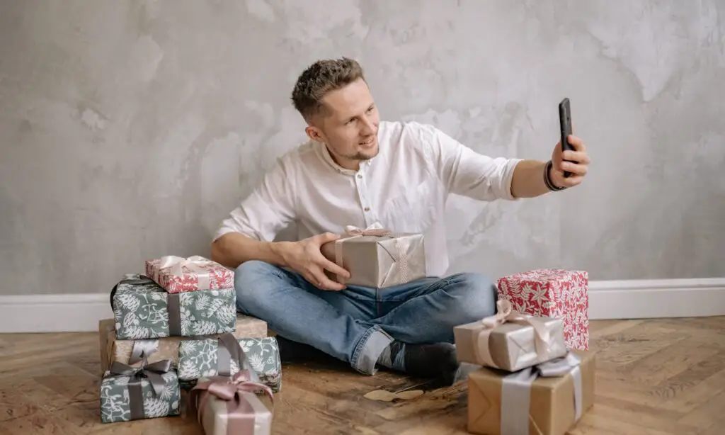 A man takes a selfie with boxes of wrapped gifts